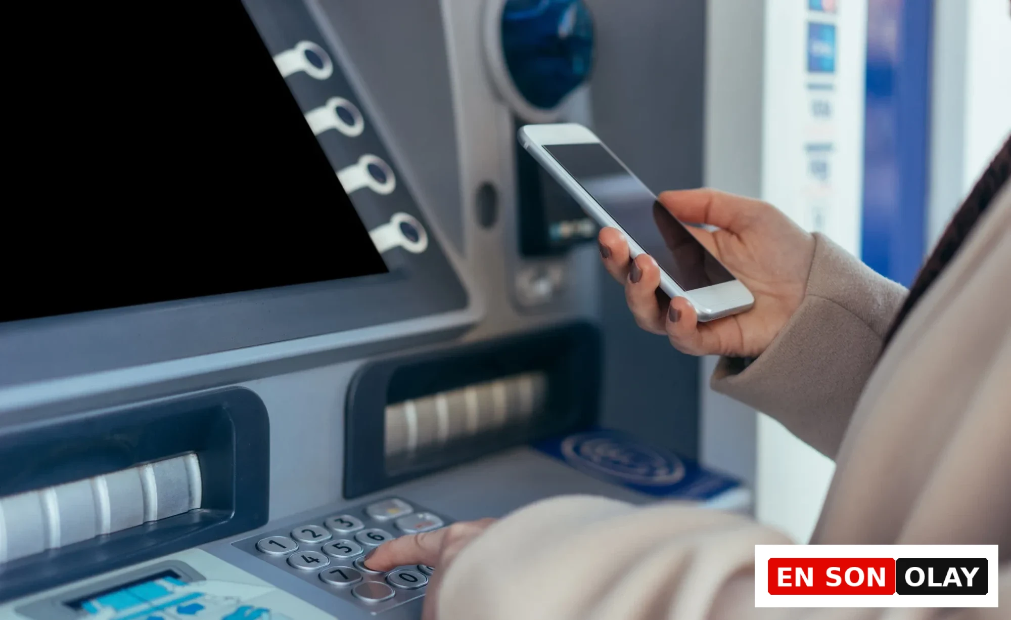ATM'de tuş takımına basan ve akıllı telefon tutan bir kişinin yakın plan görüntüsü, Nisan ayında Aslan burcunun finansal durumunda beklenen kazançları ve sürpriz artışları temsil ediyor.