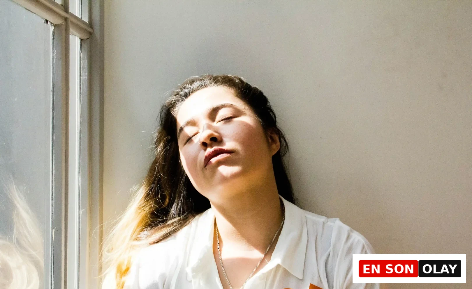 Yüzüne vuran güneş ışıklarıyla gözleri kapalı dinlenen, başını geriye yaslamış genç bir kadın, folik asit eksikliğinin yol açabileceği yorgunluk ve halsizlik gibi durumları düşündürerek beslenme dengesinin sağlığımız için ne kadar kritik olduğunu gösteriyor.