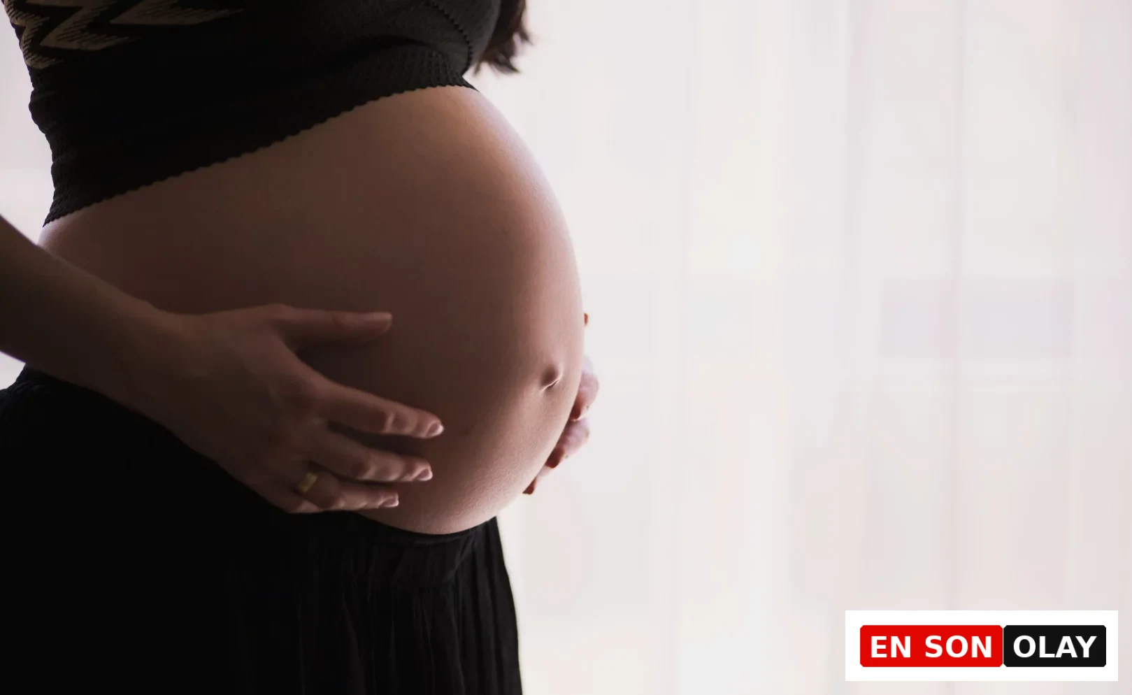 Hamilelik sürecinde bebek sağlığı ve gelişimi için hayati öneme sahip folik asit takviyesinin faydalarını anlatan bu görselde, anne adayının elleriyle karnını şefkatle okşadığı yakın çekim bir an yansıtılıyor.