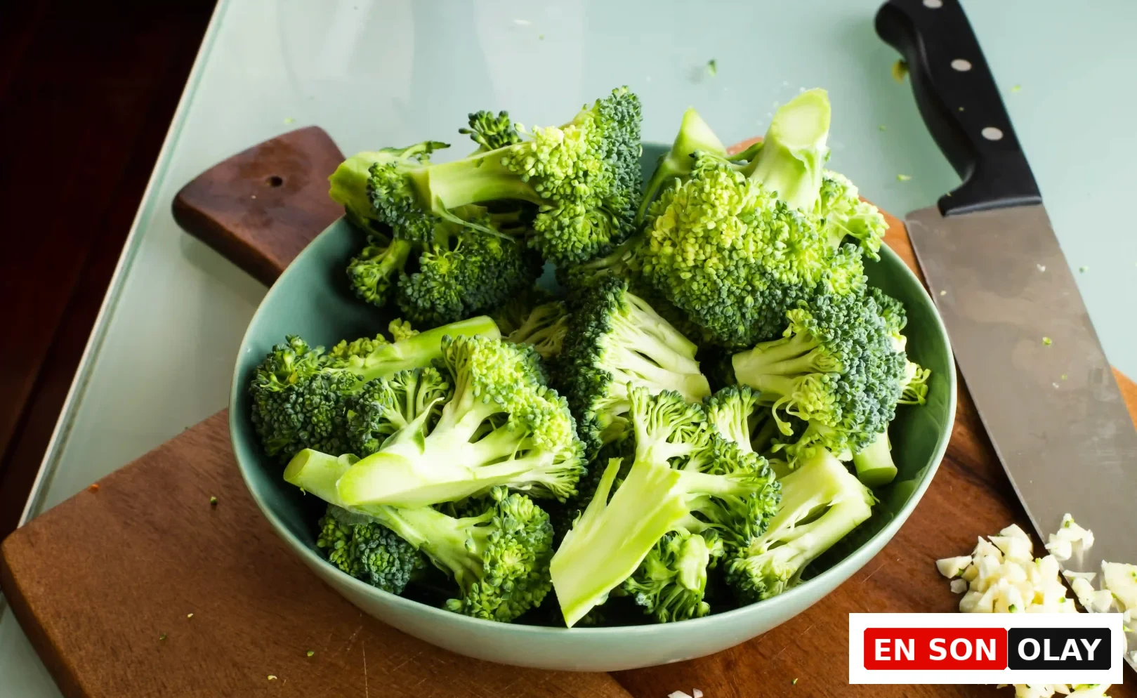 Ahşap bir kesme tahtası üzerinde, folik asit açısından zengin, taze ve canlı yeşil brokoli parçalarıyla dolu açık camgöbeği renkte bir kase, doğal yollarla B9 vitamini alımının ve sağladığı birçok faydanın altını çizerek eksiklik riskini azaltıyor.