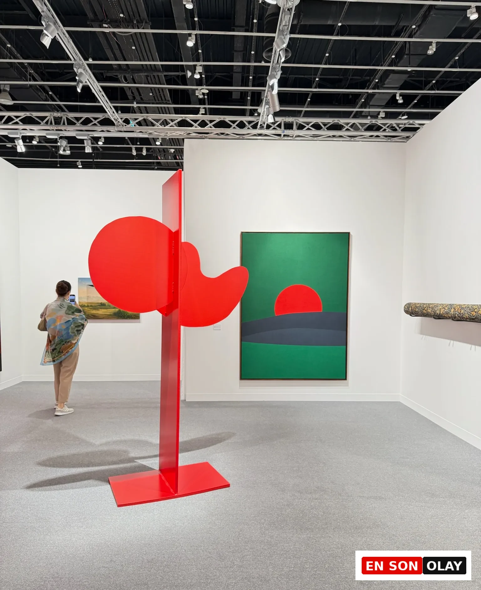 Abu Dhabi Art’ta kırmızı heykel yerleştirmesi ve arka planda geometrik kompozisyonlu çağdaş resimlerin yer aldığı sergi alanı