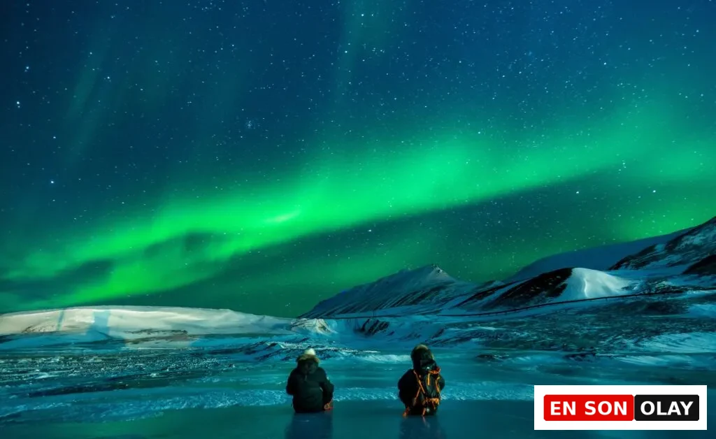 Grönland’da kuzey ışıkları altında buzlarla kaplı bir ovada oturan gezginler. Sıra dışı ve büyüleyici bir atmosfer