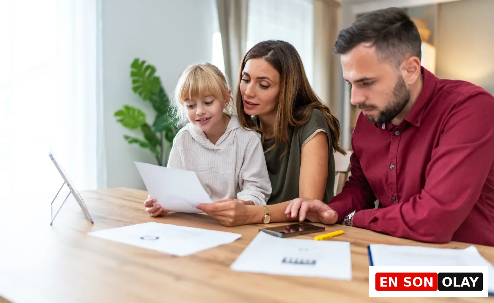 Çocuklarının finansal geleceği için bilinçli adımlar atmak isteyen bir anne ve baba, evlerinde kızlarıyla birlikte belgeleri ve dijital ekranı dikkatle inceleyerek finansal okuryazarlık ve uzun vadeli birikim konularını öğreniyorlar.