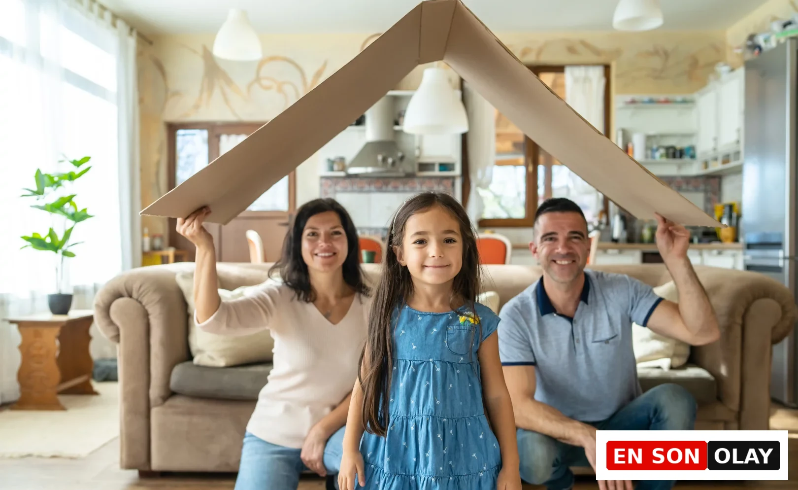 Çocuklarının geleceği için finansal okuryazarlığın önemine vurgu yapan bir anne ve baba, evlerinin sıcak atmosferinde küçük kızlarının başının üzerinde kartondan bir çatı tutarak onun için güvenli bir yuva inşa etmenin simgesel anlamını neşeyle ifade ediyor.