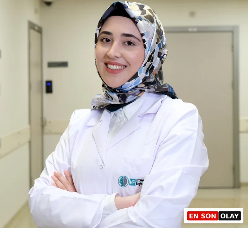 Uzman Klinik Psikolog Zeynep Betül Alp, beyaz önlüğü ve desenli başörtüsüyle hastane koridorunda gülümseyerek kollarını kavuşturmuş, kaliteli uyku için bilinçaltının ve rüyaların önemini vurgulayan bilim destekli ipuçları sunuyor.