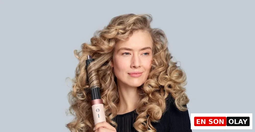 Açık gri bir fonda, altın sarısı, hacimli bukleleri olan bir kadın, saçının bir tutamını Dyson Airwrap saç şekillendiricinin Coanda hava akımıyla etrafına sararak şekillendirirken hafifçe sağa bakıyor.