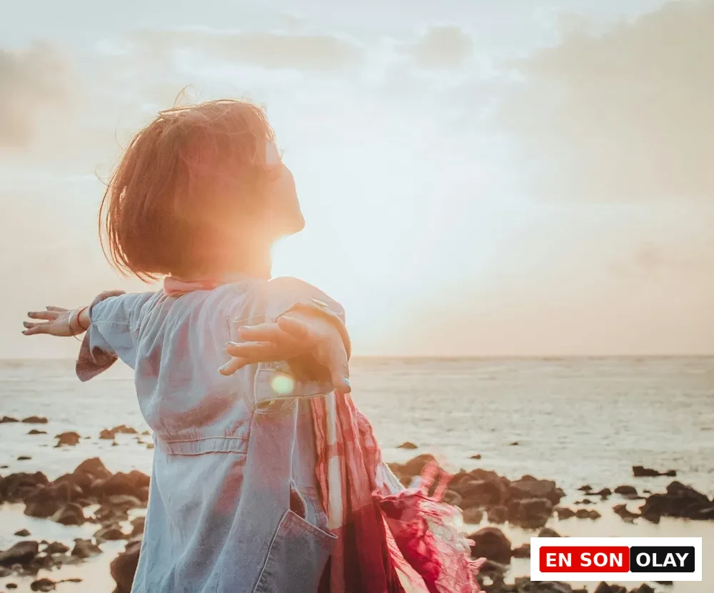 Gün batımında deniz kenarında kollarını açmış bir kadın, bedensel rahatlama ve zihinsel ferahlık hissini çağrıştırıyor.
