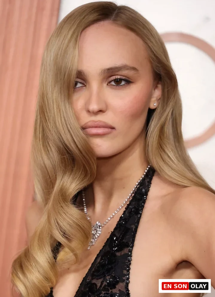 Lily-Rose Depp, yana ayrılmış, yüzünü çerçeveleyen ve omzuna dökülen belirgin iri dalgalara sahip sarı saç modeliyle dikkat çekerken, derin V yakalı siyah dantel ve payet işlemeli üstü ile ışıltılı bir kolye takıyor.