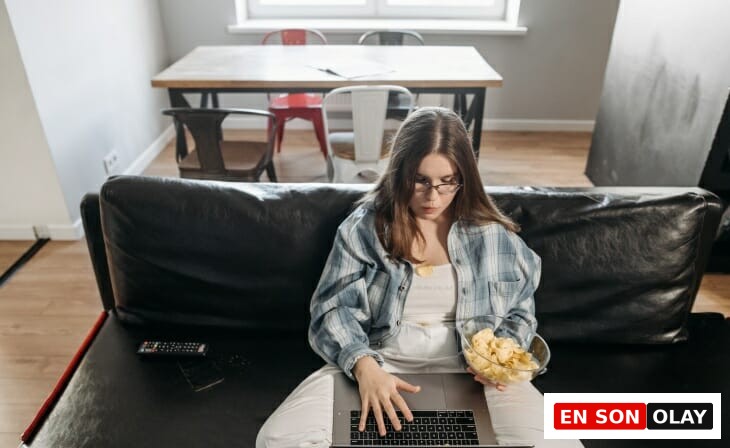 Evden çalışırken siyah deri kanepede bağdaş kurmuş, elinde cips kasesi ve kucağında dizüstü bilgisayarıyla işine odaklanmaya çalışan gözlüklü genç bir kadın, verimli olmanın püf noktalarını arıyor gibi görünüyor.