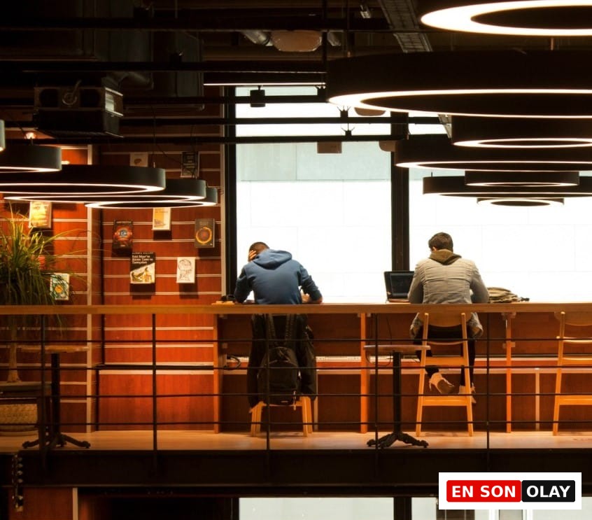 Geniş bir pencere önünde, sırtları dönük iki uzaktan çalışanın dizüstü bilgisayarlarıyla yoğunlaştığı, kitap rafları ve modern endüstriyel tavan aydınlatmalarıyla donatılmış bu ahşap masalı iç mekân, İstanbul'daki en iyi çalışma mekânları arasında huzurlu ve ilham verici bir alternatif sunuyor.