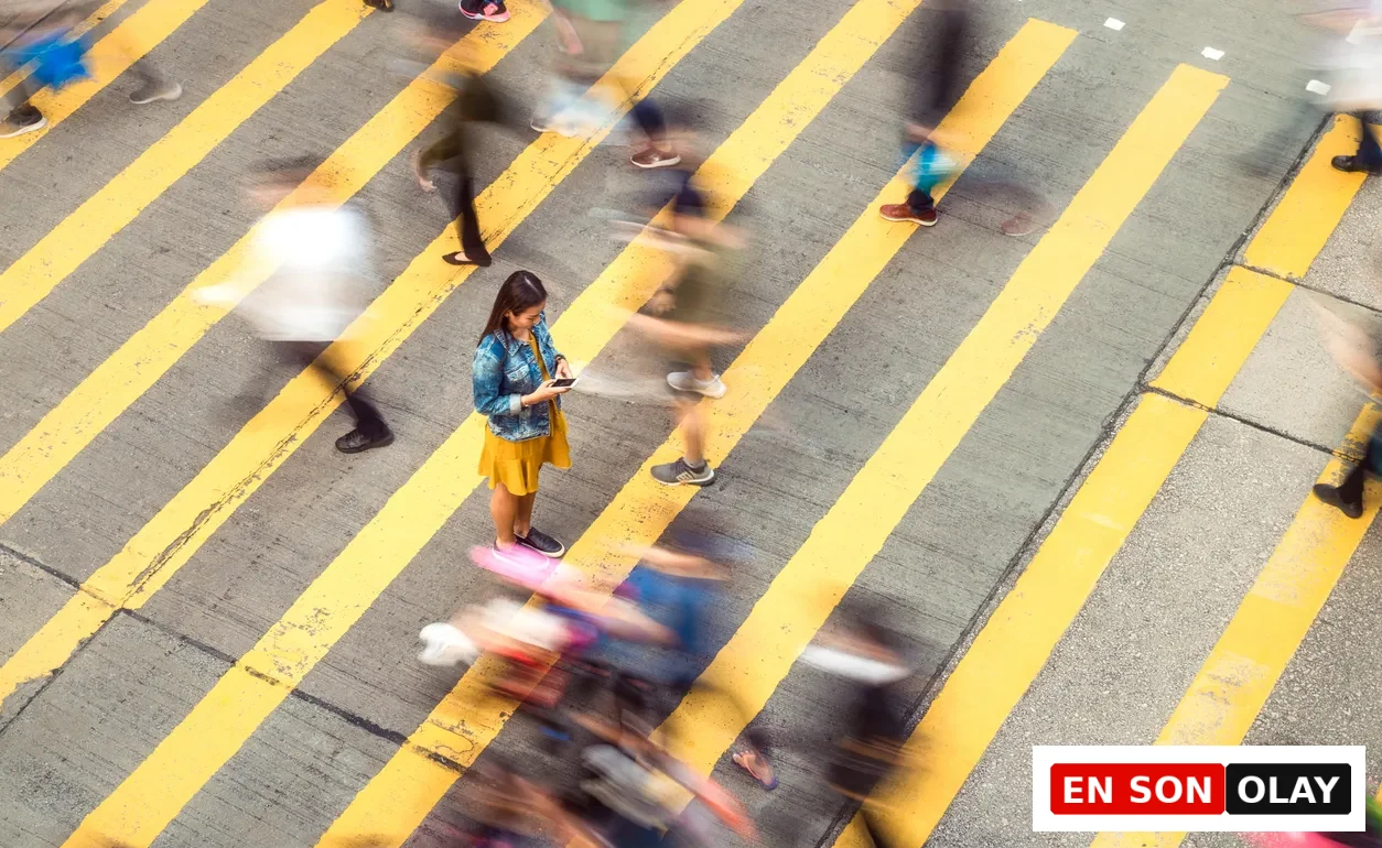 Ensonolay, Festina Lente: Hız Çağında Kontrolü Hatırlatan Antik Felsefe. Sarı şeritli yaya geçidinde hızla akan bulanık kalabalığın tam ortasında, hareketsiz durup telefonuna odaklanan bir kadın. Bu zıtlık, modern yaşamın kaosunda zihinsel dengeyi ve bilinçli duraklamayı temsil ediyor.