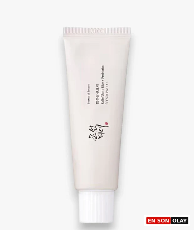 Aydınlık beyaz bir zeminde hafifçe gölgelenmiş, krem rengi, dik duran Beauty of Joseon Relief Sun: Rice + Probiotics SPF50+ PA++++ güneş kremi tüpü, markanın zarif kaligrafi logosu ve pirinç ile probiyotik içeriğini vurgulayan bilgileriyle dikkat çekiyor; cilt için etkili bir güneş koruması sunan bu ürün, beyaz, yivli bir kapakla tamamlanmıştır.