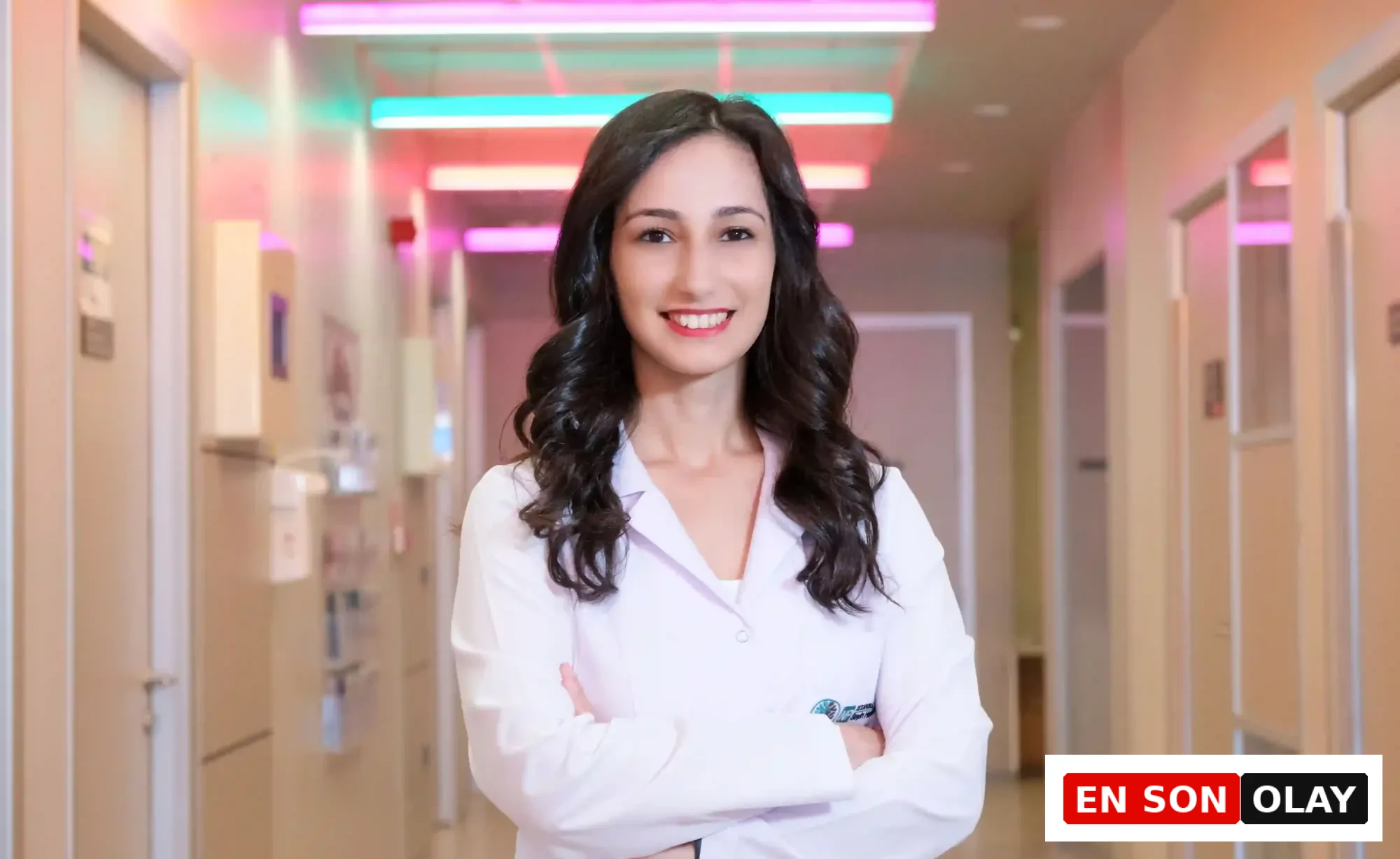 Beyaz önlüklü, kolları bağlı gülümseyen genç bir doktor, yaban mersini hakkında bilimsel bilgiler ve besin değeri üzerine rehberlik sunmak üzere modern ve renkli ışıklarla aydınlatılmış bir hastane koridorunda duruyor.