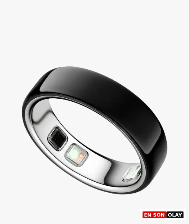 Parlak siyah dış yüzeye ve iç kısmında kalp atış hızı, uyku ve aktivite takibi gibi özellikler sunan gelişmiş biyometrik sensörlere sahip, minimalist tasarımlı bir Oura akıllı yüzük, ışık yansımasıyla beyaz bir zeminde zarifçe duruyor.