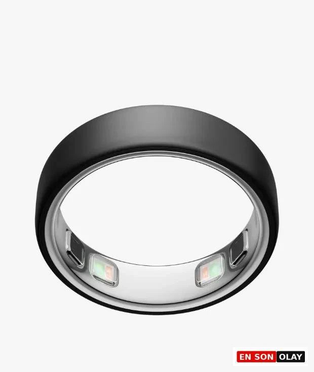 Oura Ring 5 Stealth modeli, mat koyu gri dış yüzeyine karşılık parlak gümüş rengi iç kısmında parlayan biyometrik sensörleriyle, uyku ve sağlık takibi özelliklerini vurgulayan bir akıllı yüzüğü beyaz bir zeminde çapraz bir açıyla gösteriyor.