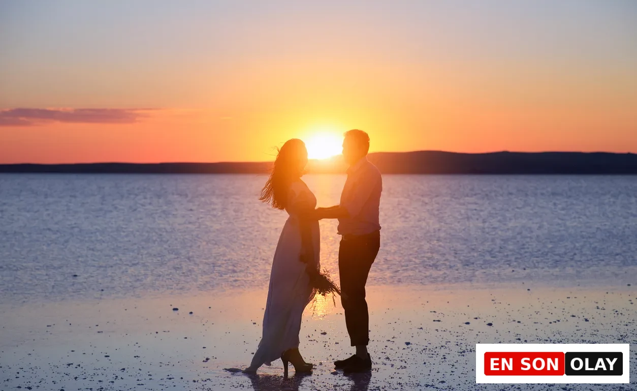 Gün batımının sıcak turuncu ve mor yansımalarıyla parlayan bir su yüzeyinde, el ele tutuşmuş, birbirlerine dönük bir çiftin silüeti, aşk ve evliliğin romantik başlangıcını kutlayan unutulmaz bir anı betimliyor.