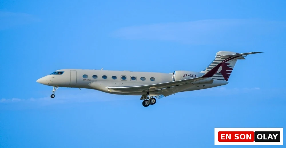 Açık mavi gökyüzünde, iniş takımları açık vaziyette alçaktan uçan, gövdesinde QATAR yazısı ve kuyruk kanadında Katar Havayolları'nın bordo renkli antilop amblemi belirgin olan modern ve şık bir özel jet.