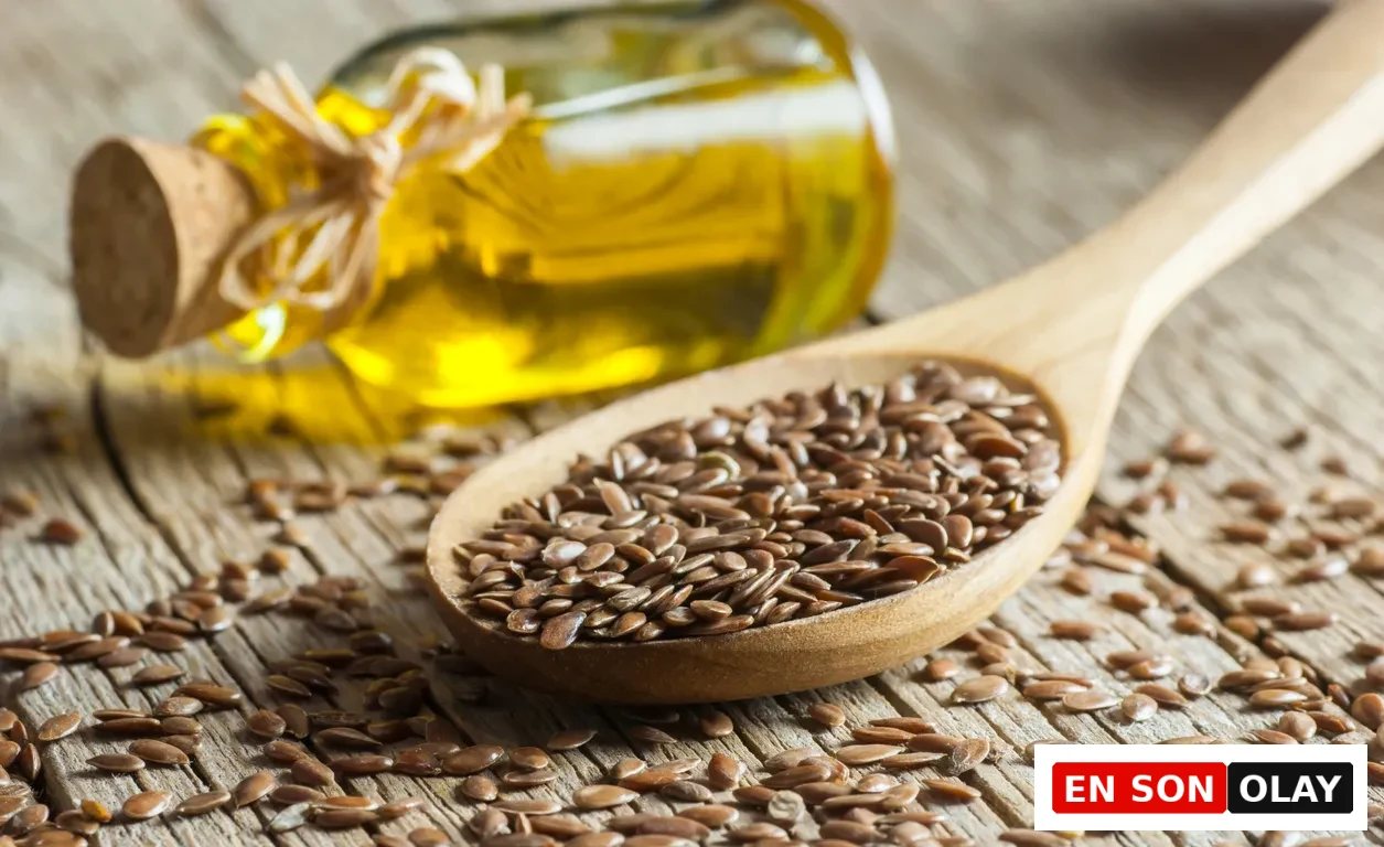 Ahşap zeminde, sağlık ve hormonal denge için önemli bir süper besin olan keten tohumunun zenginliğini gösteren bu yakın çekimde, bir kaşık dolusu parlak bütün keten tohumu ve arka planda altın rengi keten tohumu yağı şişesi dikkat çekiyor.