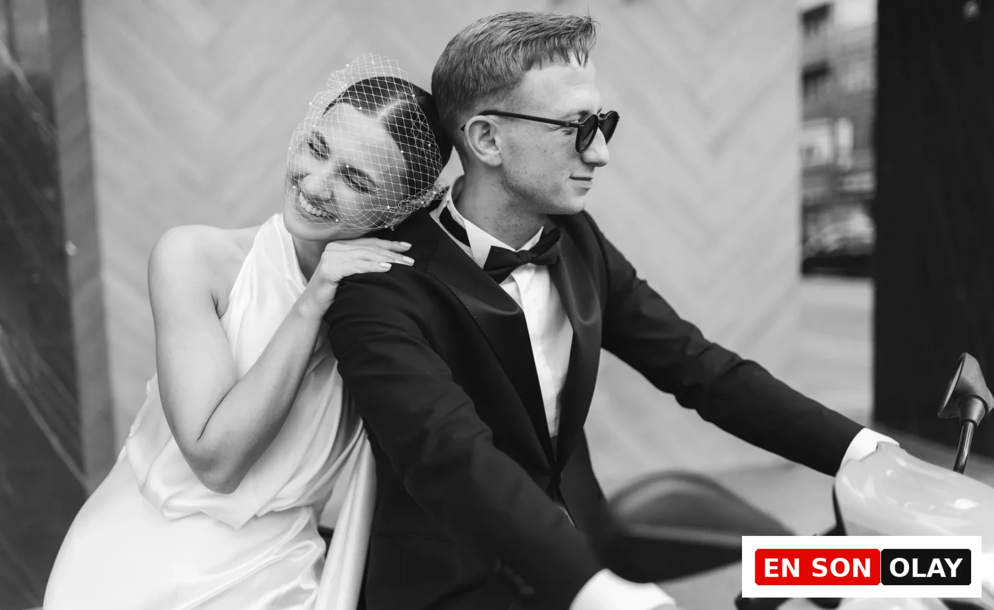 Siyah beyaz fotoğrafta, smokinli ve güneş gözlüklü bir adam scooter üzerinde otururken, neşeli bir gülümsemeyle duvaklı bir kadın omzuna yaslanmış, Terazi burcunun aşk hayatında yeni başlangıçları ve derin bağlılıkları işaret ediyor.