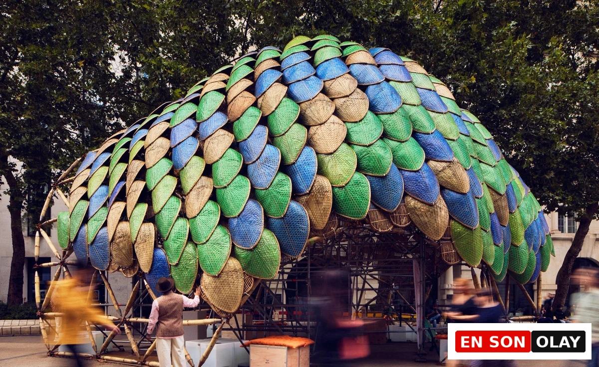 London Tasarım Festivali'nde sergilenen Studio Saar ve Atelier One'ın The Pangolin Shield enstalasyonu, bambu strüktür üzerine monte edilmiş yeşil, mavi ve doğal renklerdeki pullu panelleriyle dikkat çekerek, çevresindeki kalabalığı ağırlayan dev bir dış mekân yapısıdır.
