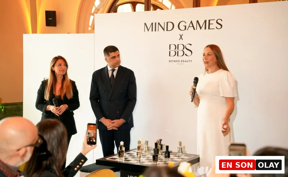 Mind Games Parfüm Kurucusu Alex Shalbaf, şık koyu renk takım elbisesiyle modern bir ofis masasında oturmuş, elleri kenetli bir şekilde kameraya sıcak bir ifadeyle bakarak gülümserken, röportajı için poz veriyor.