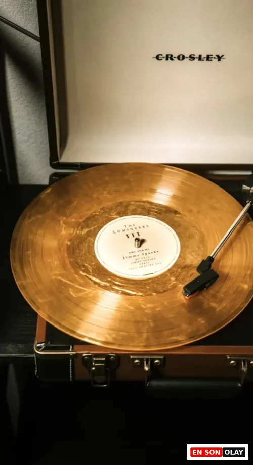 CROSLEY marka taşınabilir bir pikapta çalan, üzerinde The Lumineers III yazılı etiketiyle dikkat çeken, parıltılı altın rengi bir plağın yakın çekim görüntüsü, müzikseverler arasında neden bu kadar popüler olduğunu gösteren bir listening room deneyimini gözler önüne seriyor.