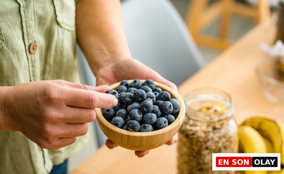 Ahşap kasede taze yaban mersini tutan bir kadının elleri ve arka planda muesli kavanozu.