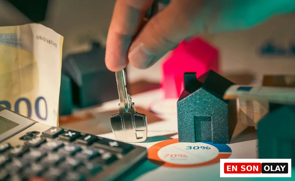 Elinde anahtar tutan bir elin, minyatür ev modelleri, 200 Euro banknotu, hesap makinesi ve yüzde oranları içeren finansal grafikle dolu bir masanın üzerinde duruşu, gayrimenkul yatırımlarının reel faiz oranlarıyla ilişkisini ve maliyetlerini hesaplama ihtiyacını vurguluyor.