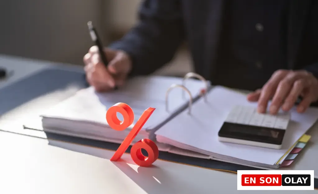 Finansal analiz ve reel faiz hesaplamaları bağlamında, bir masa üzerinde açık bir defterdeki belgelere not alan ve hesap makinesi kullanan kişinin elleri ile ön planda duran belirgin turuncu yüzde işareti.