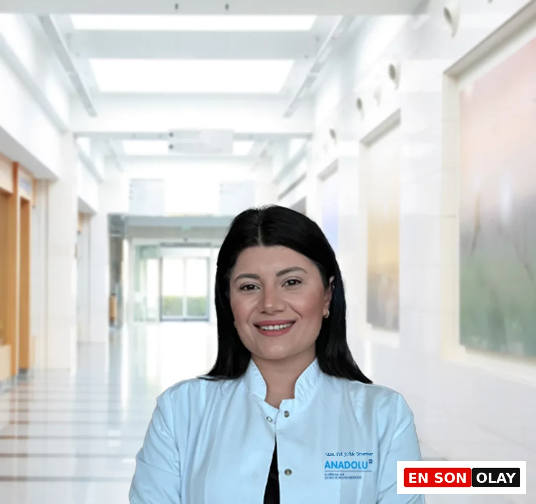 Uzman Psikolog Jülide Unutmaz, modern bir hastane koridorunun aydınlık atmosferinde beyaz önlüğüyle güven veren bir gülümsemeyle durarak, Tükenmişlik Sendromu ve İş Yeri Deformasyonu hakkında makalede okuyuculara rehberlik ediyor.