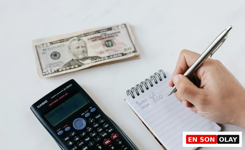 Bir kişi, vergi ve kredi notlarını deftere yazarken yanında bir hesap makinesi ve 50 dolarlık banknotlar bulunuyor.