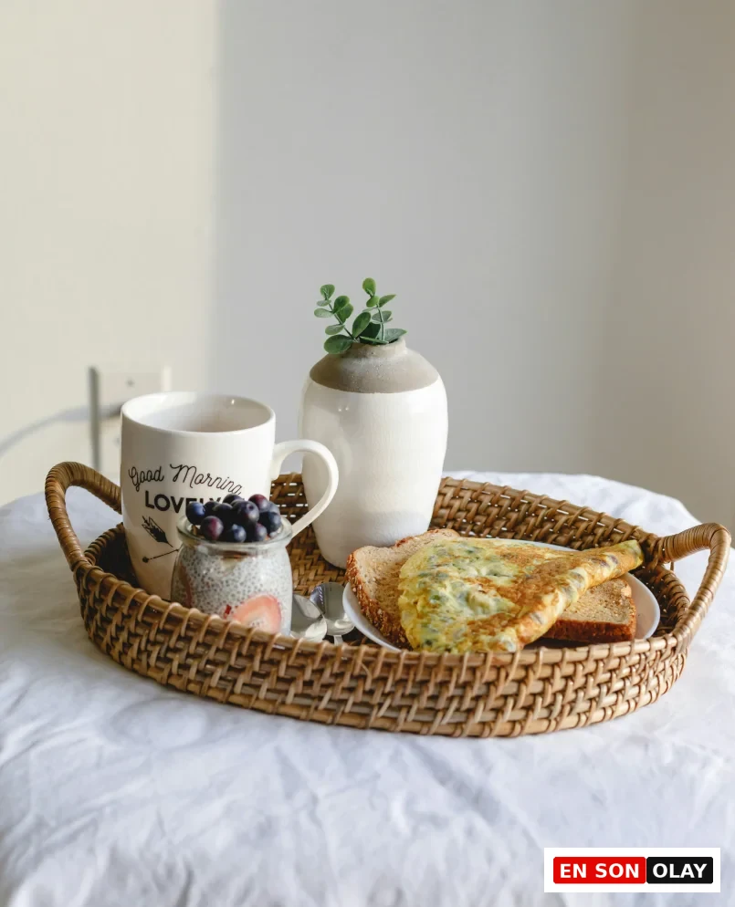Hasır bir tepside, üzerinde Good Morning Love yazılı beyaz bir kupa, yaban mersini ve çilekli chia puding, yeşillikli omlet ve iki dilim kızarmış ekmek gibi çeşitli yiyeceklerin düzenli ve davetkar bir şekilde sunulduğu bir kahvaltı, mindful beslenme pratiklerinin dinginliğini ve yavaşlama adımlarını temsil ediyor.
