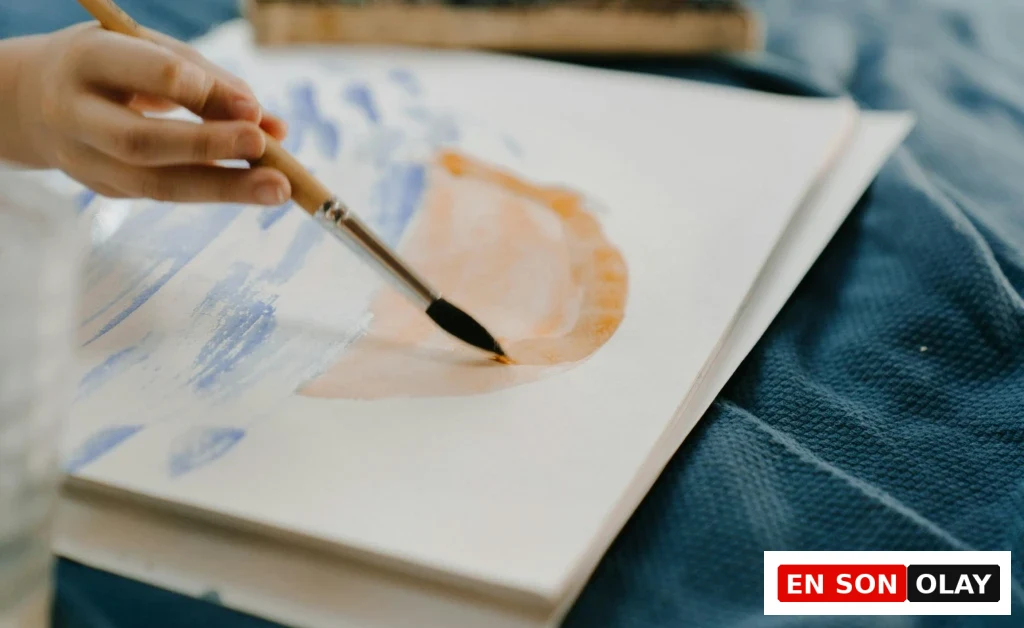 Bir çocuğun sanat terapisi sırasında fırçayla pastel tonlarda su bazlı boya çalışması yapması.